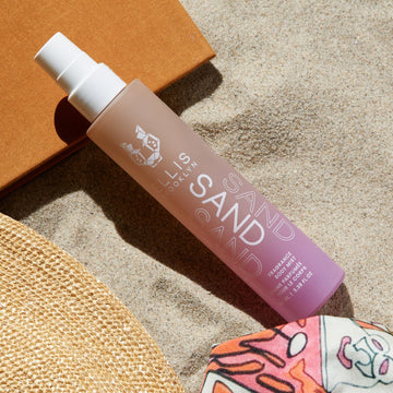 Sand Hair and Body Fragrance Mist 100ml in sand and orange book next to straw hat, and pink, white, and orange scarf.