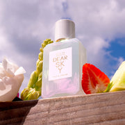 Dear Sky 50ml Eau de Parfum sur un morceau de bois à côté de fraise, melon et fleurs, avec le ciel et les nuages en arrière-plan.