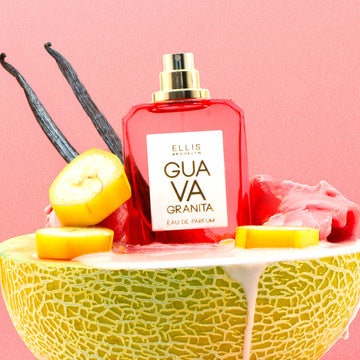 Guava Granita 50ml Eau De Parfum with cap removed on halved melon with pink sorbet, sliced banana, and vanilla beans against pink background.