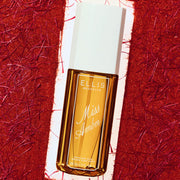 Brume parfumée Miss Amber, flacon de 90 mL avec un corps en verre ambré et un bouchon blanc, posé sur un fond texturé rouge et blanc.