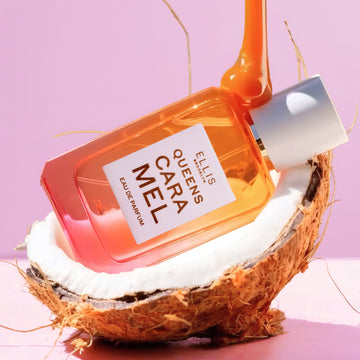 QUEENS CARAMEL Eau de Parfum 50ml posé dans une moitié de noix de coco avec du caramel dégoulinant sur le flacon sur un fond rose