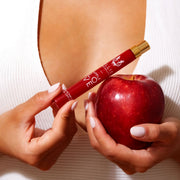 Mannequin avec du vernis à ongles rose clair portant une chemise blanche, tenant le spray de voyage Apple Love 10ml Eau De Parfum dans une main et une pomme dans l'autre main, près de la poitrine.