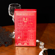 Boîte du coffret découverte de parfum Red An Ellis Brooklyn Mystery sur une table en bois avec un collier en diamant, un bracelet noir et blanc, un masque en dentelle noire et un verre à pied, sur fond noir.