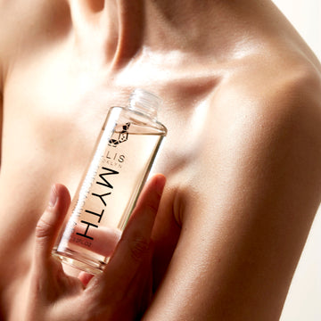 Modèle tenant l'huile corporelle parfumée spectaculaire Myth 95 ml sans bouchon, près de la clavicule, sur fond blanc.