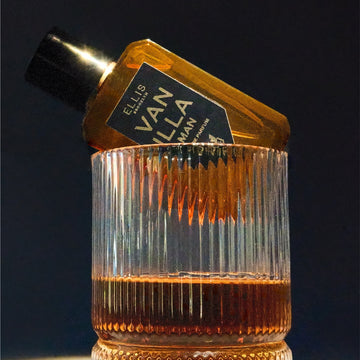 Vanilla Man 50ml Eau De Parfum sitting on rim of glass of whiskey, on black background.