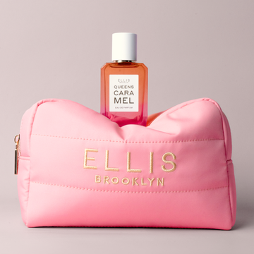 Trousse de maquillage rose avec broderie dorée portant la mention « Ellis Brooklyn » avec QUEENS CARAMEL Eau de Parfum 50ml posée dessus sur fond gris