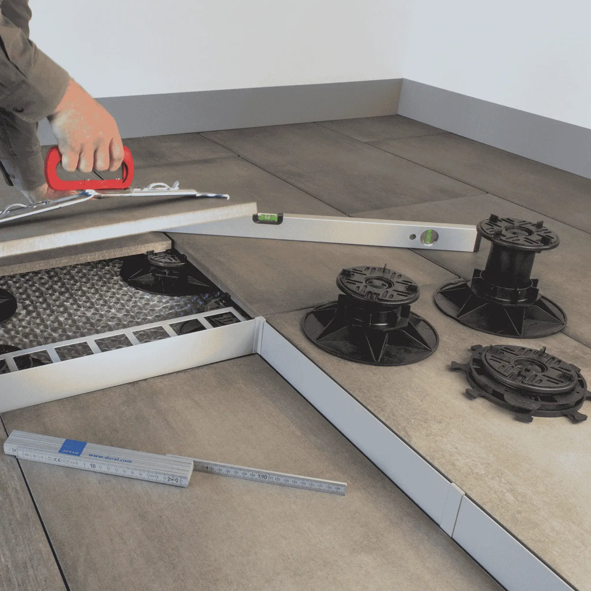Lifestyle image of the 3 different pedestal sizes on a terrace. The tradesman uses a spirit level and a slab lifter to lay tiles.