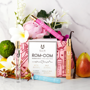 Vaporisateur de voyage Florist 10 ml Eau de Parfum sur un sac de coffret cadeau parfumé Rom-Com avec motifs rouges et roses, Myth 10 ml Eau de Parfum Vaporisateur de voyage, Salt 10 ml Eau de Parfum Vaporisateur de voyage, et Vanilla Milk 10 ml Eau de Parfum Vaporisateur de voyage sur un décor en marbre blanc et gris avec des fleurs blanches, roses, violettes et jaunes, bois de santal, citron, poire et bergamote.