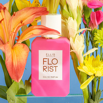 Florist Eau De Parfum on glass block against blue background surrounded by pink, white, green, yellow, and orange flowers.
