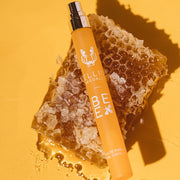 Bee 10ml Eau De Parfum Travel Spray with cap removed resting on piece of honeycomb, on yellow background.